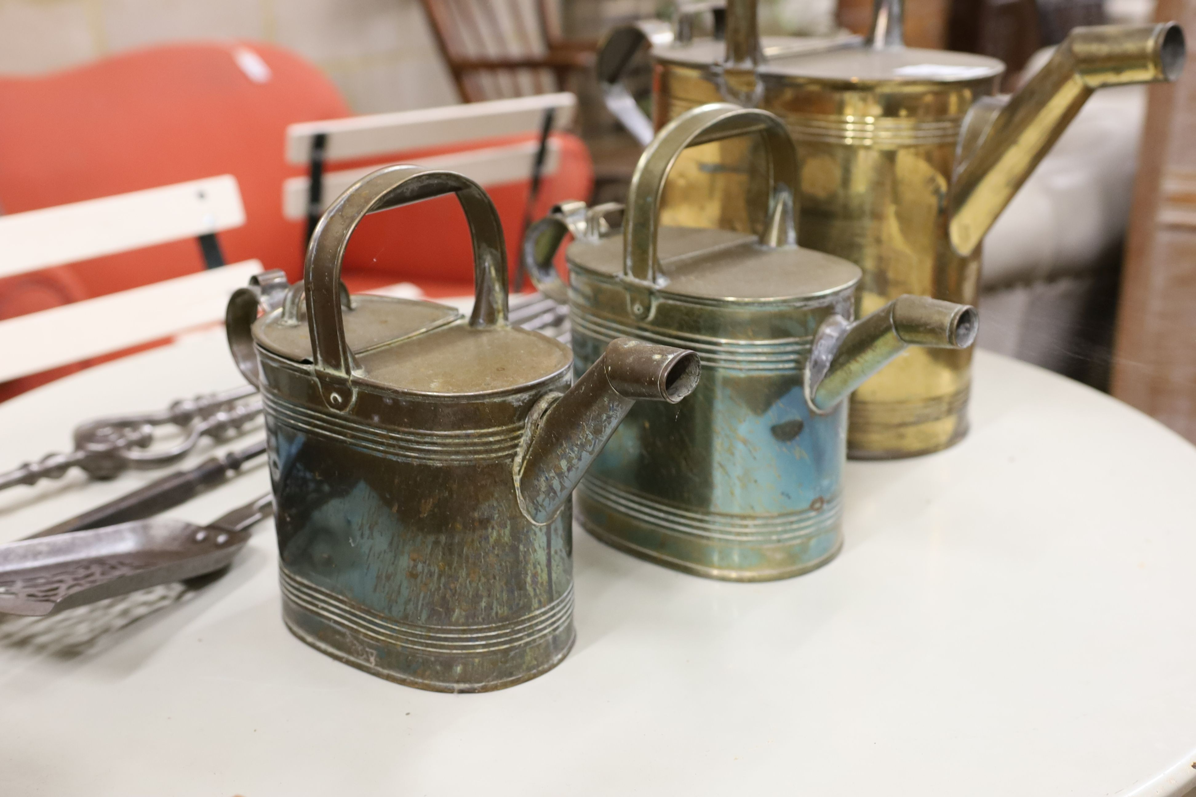 Three graduating brassed metal watering cans, largest height 40cm, together with a set of cast iron fire implements